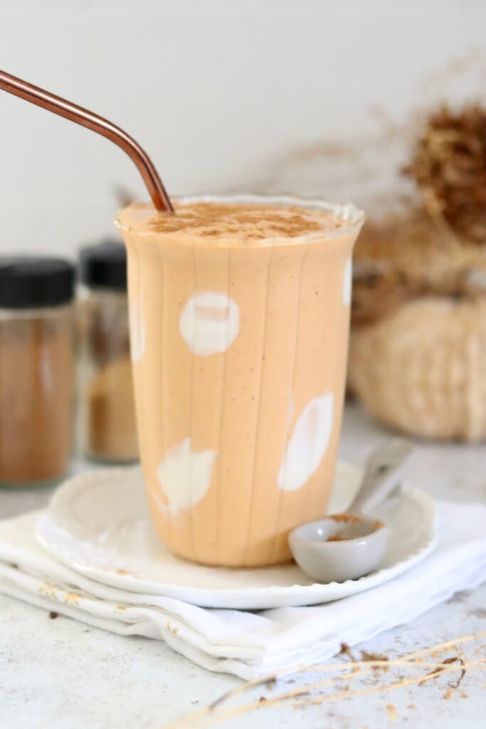 Pumpkin smoothie topped with spice beside a small dish of cinnamon