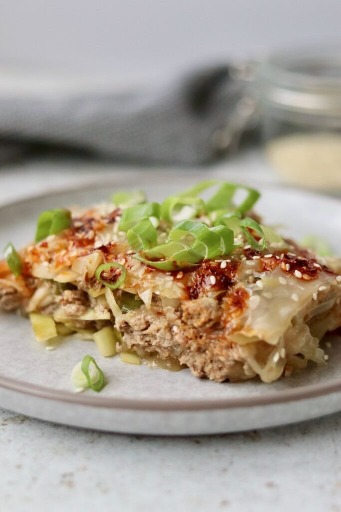 Plated rice paper lasagna slice topped with chilli crisp, spring onion and sesame seeds