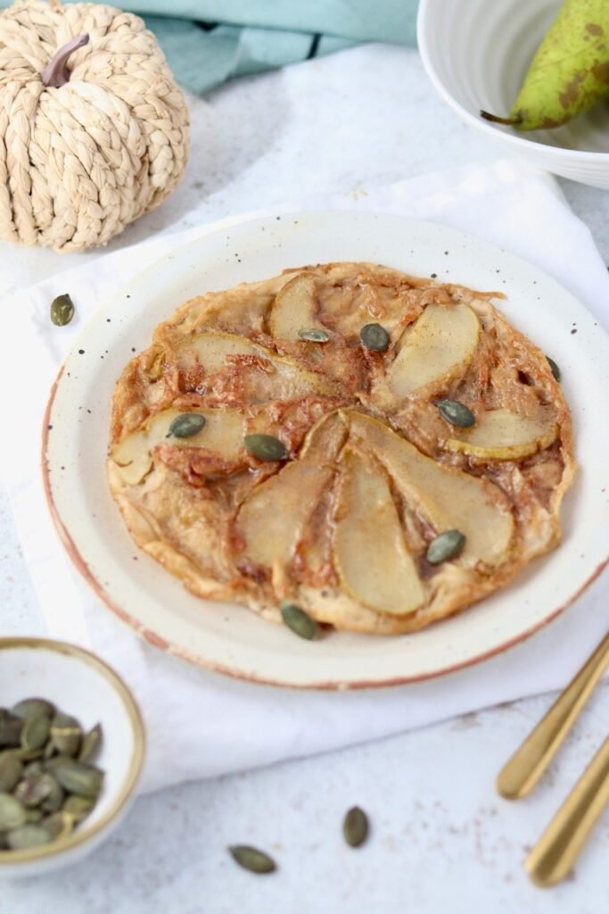 Whole rice paper tarte tatin plated with caramelised pear slices and toasted pumpkin seeds