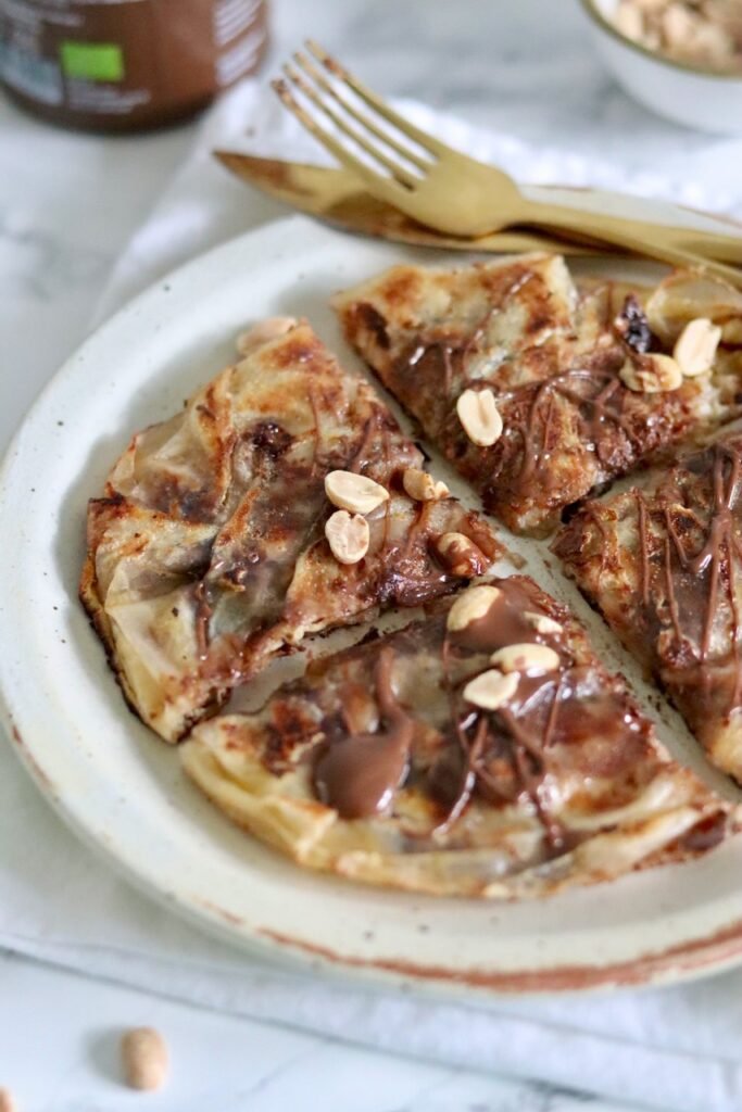 Snickers rice paper crepe sliced on a plate with chocolate drizzle and chopped peanuts