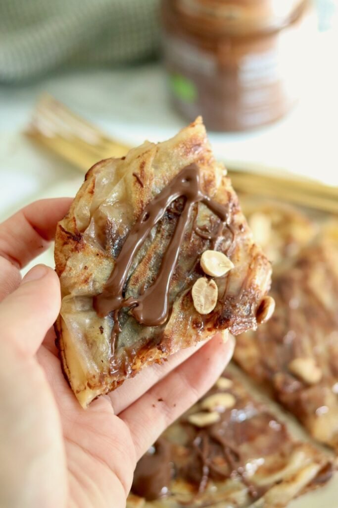 Hand holding a slice of snickers rice paper pancake showing the soft banana centre