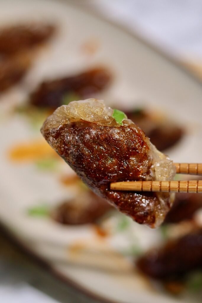 Chopsticks lifting a teriyaki duck dumpling above the platter