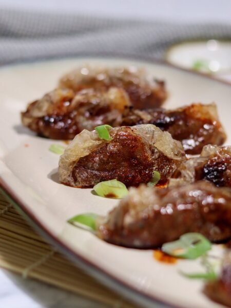Crispy teriyaki duck dumplings on a cream platter with spring onion and chilli oil