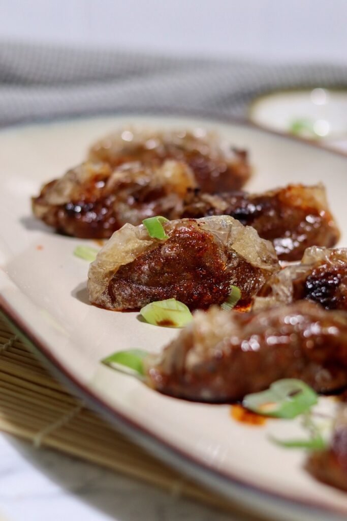 Crispy teriyaki duck dumplings on a cream platter with spring onion and chilli oil