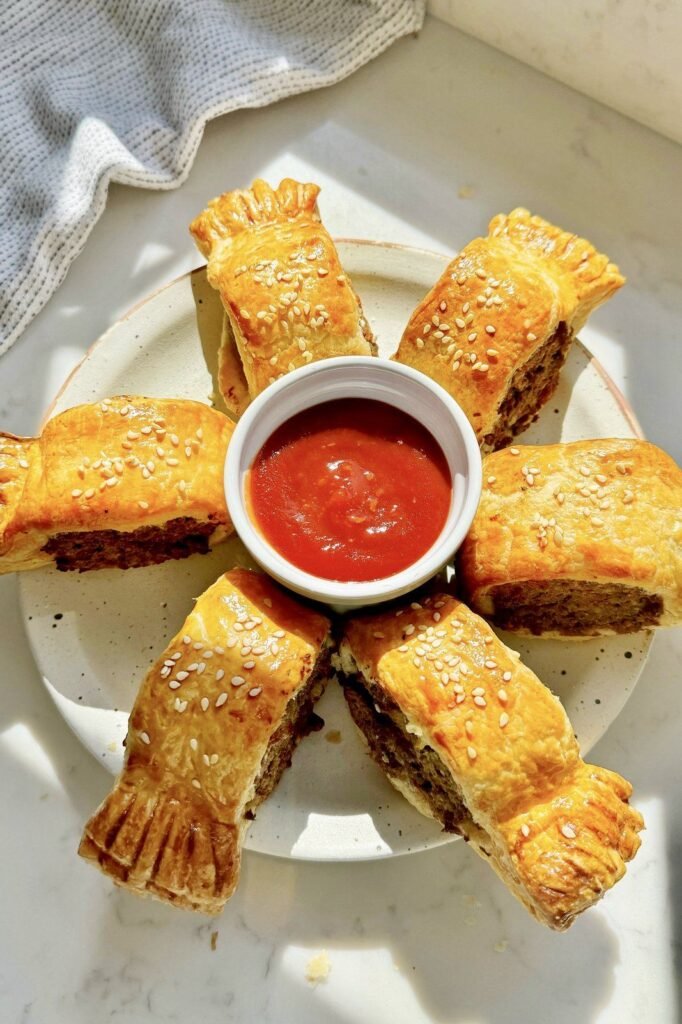 Golden vegetarian sausage rolls with sesame seeds around a pot of ketchup