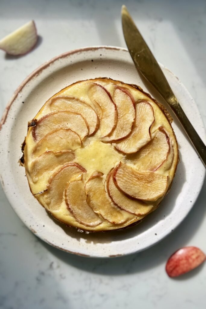 Whole flourless apple cake with a spiral of baked apple slices on a speckled plate