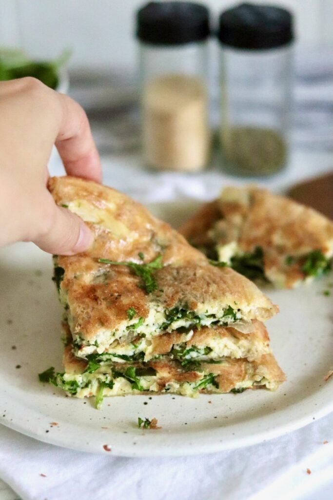 Lifting a slice of gluten free spinach and feta pie from a stack