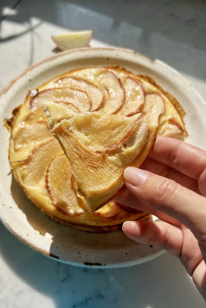 Hand lifting a slice of healthy apple cake made with almond flour, with fanned apple slices on top