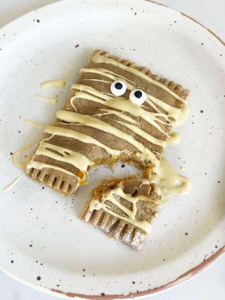 Healthy pumpkin pop tart decorated as a mummy with white chocolate drizzle, bitten to show the pumpkin filling