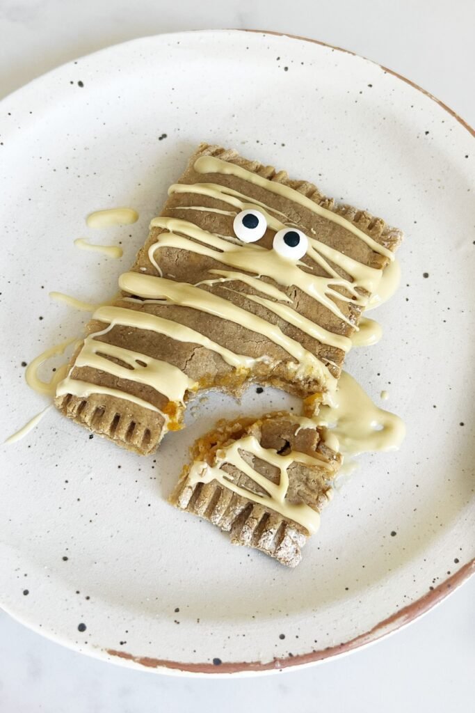 Healthy pumpkin pop tart decorated as a mummy with white chocolate drizzle, bitten to show the pumpkin filling