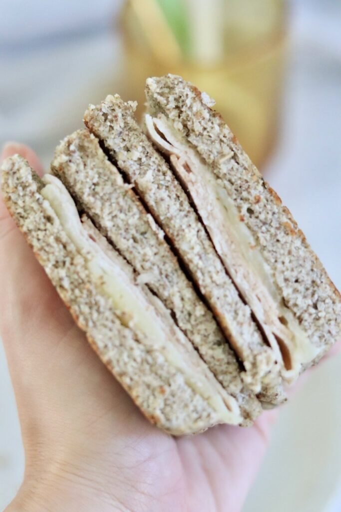 Holding a chia seed keto bread sandwich with turkey and melted cheese