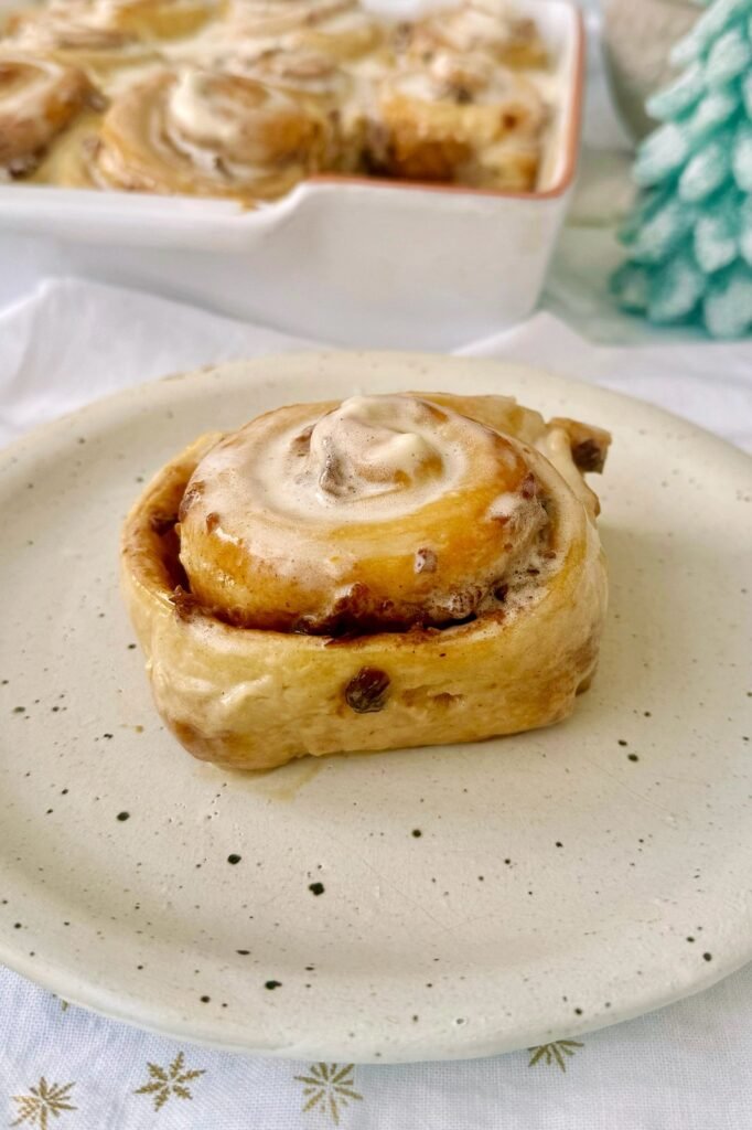 A Christmas cinnamon roll with brandy cream on a festive plate