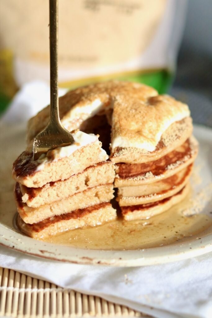 A fork cutting into a stack of roasted soybean flour pancakes topped with Greek yogurt and konggaru