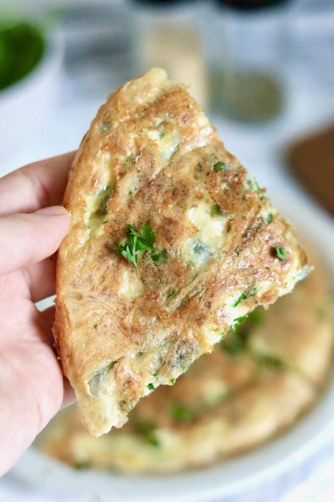 Hand holding a crispy wedge of spinach and feta rice paper pie