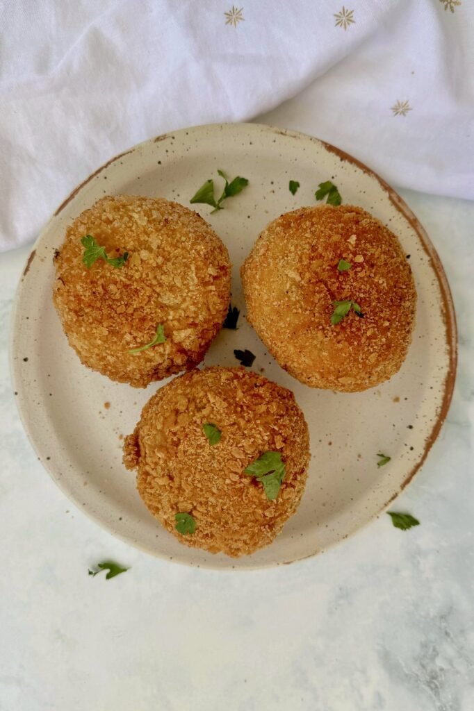 Three golden turkey scotch eggs on a plate with fresh parsley